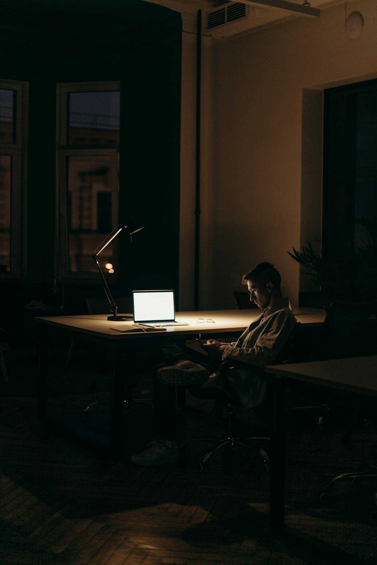 Person sitting in dark room alone at his their desk.
